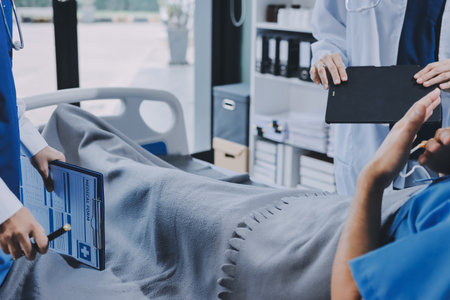 A young man lies on a bed in a hospital ward talking with her young Indian doctor. Doctor checking...