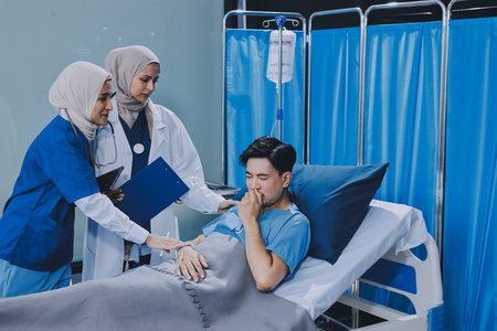 A young man lies on a bed in a hospital ward talking with his doctor. Doctor checking patient's health and treating patient.の写真素材