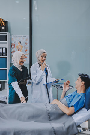 A young man lies on a bed in a hospital ward talking with his doctor. Doctor checking patient's health, hospital admission of patientの写真素材