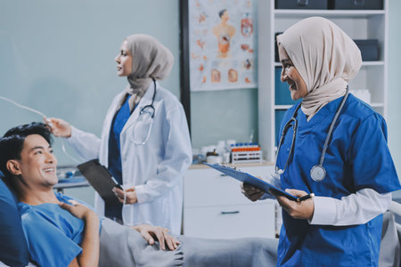 A young man lies on a bed in a hospital ward talking with her young Indian doctor. Doctor checking...