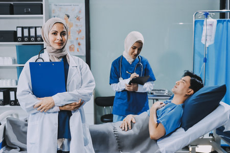 A young man lies on a bed in a hospital ward talking with his doctor. Doctor checking patient's health, doctor treating patient, hospital admission of patientの写真素材