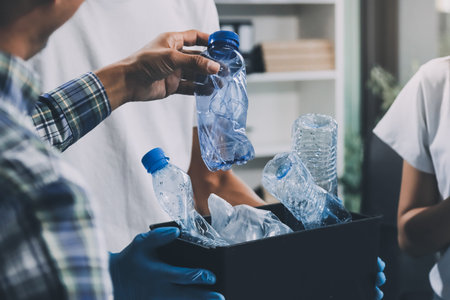 Close-up of female hands from a family collecting plastic waste and bottles from the ground. They wear gloves and focus on recycling to help reduce plastic pollution and protect the environment.の写真素材