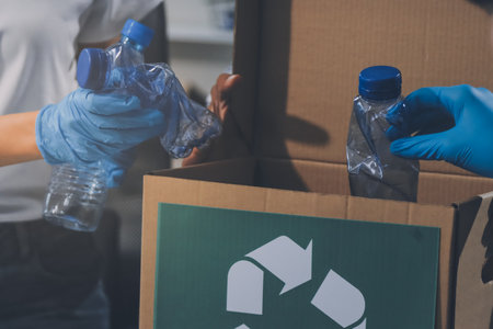 Close-up of female hands from a family collecting plastic waste and bottles from the ground. They wear gloves and focus on recycling to help reduce plastic pollution and protect the environment.の写真素材