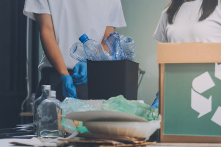 Close-up of female hands from a family collecting plastic waste and bottles from the ground. They wear gloves and focus on recycling to help reduce plastic pollution and protect the environment.の写真素材