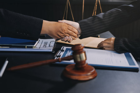 Two lawyers shaking hands after reaching an agreement during a legal trial, with scales of justice and gavel in the foregroundの写真素材