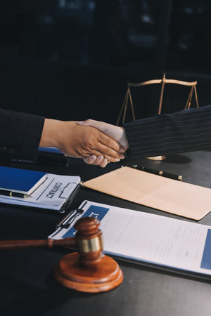 Two lawyers shaking hands after reaching an agreement during a legal trial, with scales of justice and gavel in the foregroundの写真素材