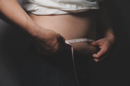 Asian man in front of a mirror looks at his body. Excess belly fat, Unhealthy lifestyle, Diet concept.の写真素材