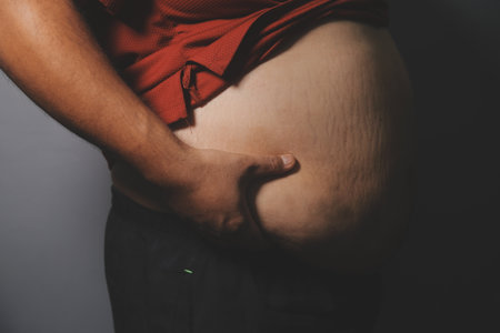 Asian man in front of a mirror looks at his body. Excess belly fat, Unhealthy lifestyle, Diet concept.の写真素材