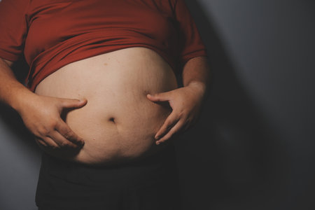 Asian man in front of a mirror looks at his body. Excess belly fat, Unhealthy lifestyle, Diet concept.の写真素材