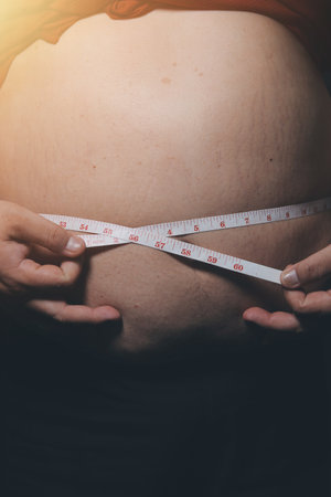 Asian man in front of a mirror looks at his body. Excess belly fat, Unhealthy lifestyle, Diet...