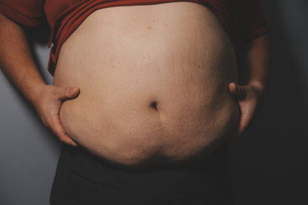Fat man in front of a mirror looks at his body. Excess belly fat, Unhealthy lifestyle, Diet concept.の写真素材