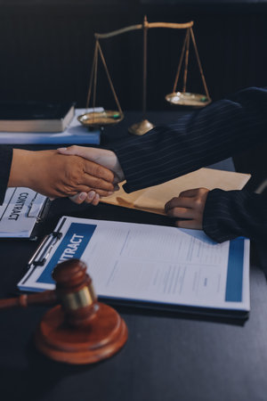 Two lawyers shaking hands after reaching an agreement during a legal trial, with scales of justice and gavel in the foregroundの写真素材