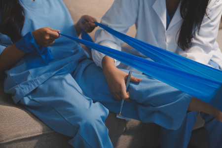 Confident physical therapist helps patient use resistance band stretching out his leg in clinic room.の写真素材