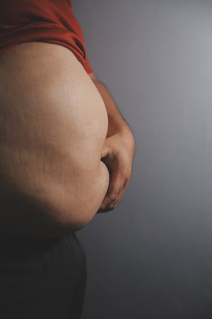 Fat man in front of a mirror looks at his body. Excess belly fat, Unhealthy lifestyle, Diet concept.の写真素材