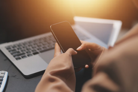 Young beautiful Asian businesswoman holding smartphone while working in the office room.の写真素材