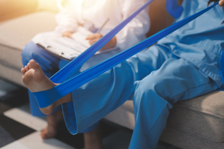 Confident physical therapist helps patient use resistance band stretching out his leg in clinic room.の写真素材