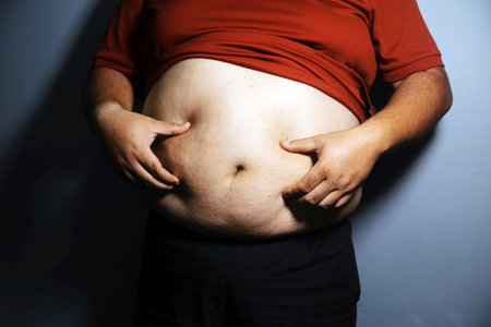 Fat man in front of a mirror looks at his body. Excess belly fat, Unhealthy lifestyle, Diet concept.
