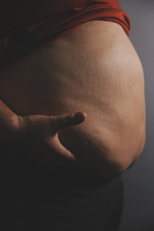 Asian man in front of a mirror looks at his body. Excess belly fat, Diet concept.