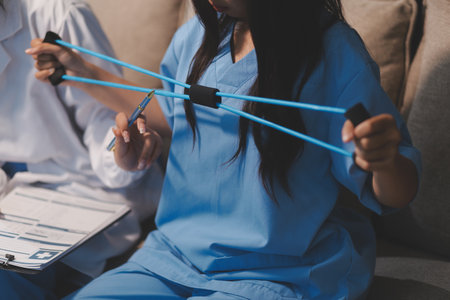 Doctor physiotherapist assisting a male patient while giving exercising treatment on stretching his arm with exercise band in the clinic, Rehabilitation physiotherapy conceptの写真素材