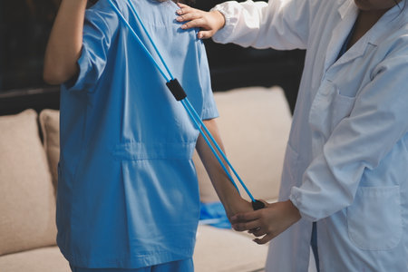 Physiotherapist assisting a male patient while giving exercising treatment on stretching his arm with exercise band in the clinic, Rehabilitation physiotherapy conceptの写真素材