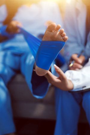 Confident physical therapist helps patient use resistance band stretching out his leg in clinic room.の写真素材
