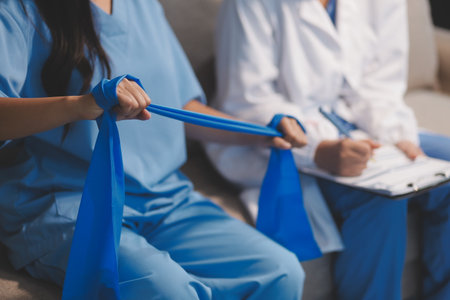 Doctor physiotherapist assisting a male patient while giving exercising treatment on stretching his arm with exercise band in the clinic, Rehabilitation physiotherapy conceptの写真素材