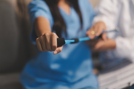Doctor physiotherapist assisting a male patient while giving exercising treatment on stretching his arm with exercise band in the clinic, Rehabilitation physiotherapy conceptの写真素材