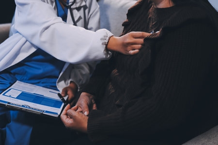 Homecare nursing service and elderly people cardiology healthcare. Close up of young hispanic female doctor nurse check mature caucasian man patient heartbeat using stethoscope during visitの写真素材