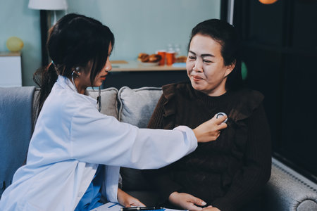 Homecare nursing service and elderly people cardiology healthcare. Close up of young female doctor nurse check mature woman patient heartbeat using stethoscope during visitの写真素材