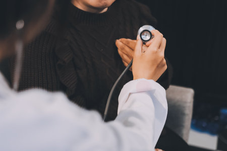 Homecare nursing service and elderly people cardiology healthcare. Close up of young hispanic female doctor nurse check mature caucasian man patient heartbeat using stethoscope during visitの写真素材