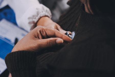 Homecare nursing service and elderly people cardiology healthcare. Close up of young hispanic female doctor nurse check mature caucasian man patient heartbeat using stethoscope during visitの写真素材