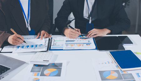 Focused young businessman signing agreement with skilled lawyer in eyeglasses. Concentrated financial advisor showing place for signature on paper contract document to male client at meeting in officeの写真素材
