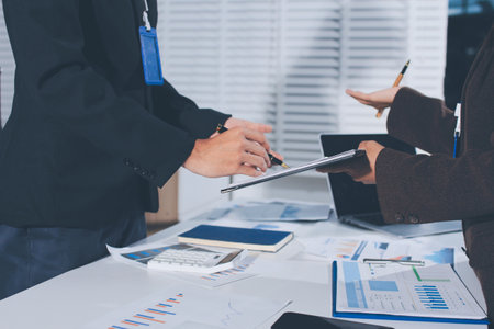 Focused young businessman signing agreement with skilled lawyer in eyeglasses. Concentrated financial advisor showing place for signature on paper contract document to male client at meeting in officeの写真素材