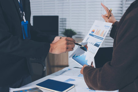 Focused young businessman signing agreement with skilled lawyer in eyeglasses. Concentrated financial advisor showing place for signature on paper contract document to male client at meeting in officeの写真素材