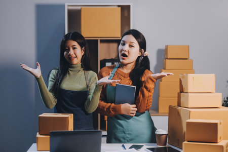 Startup SME small business entrepreneur of freelance Asian woman wearing apron using laptop and box to receive and review orders online to prepare to pack sell to customers, online sme business ideas.の写真素材