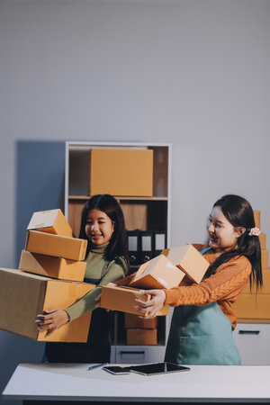 Startup SME small business entrepreneur of freelance Asian woman wearing apron using laptop and box to receive and review orders online to prepare to pack sell to customers, online sme business ideas.の写真素材