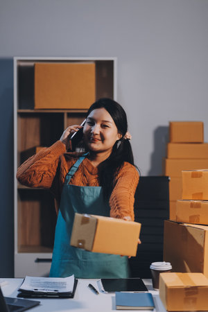 Startup SME small business entrepreneur of freelance Asian woman wearing apron using laptop and box to receive and review orders online to prepare to pack sell to customers, online sme business ideas.の写真素材