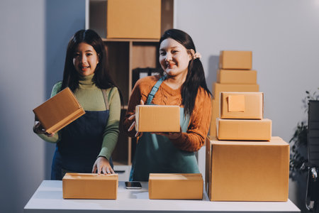Startup SME small business entrepreneur of freelance Asian woman wearing apron using laptop and box to receive and review orders online to prepare to pack sell to customers, online sme business ideas.の写真素材