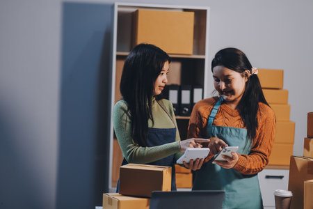 Startup SME small business entrepreneur of freelance Asian woman wearing apron using laptop and box to receive and review orders online to prepare to pack sell to customers, online sme business ideas.の写真素材