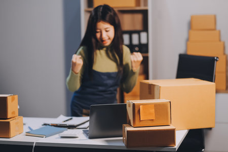Startup SME small business entrepreneur of freelance Asian woman wearing apron using laptop and box to receive and review orders online to prepare to pack sell to customers, online sme business ideas.の写真素材