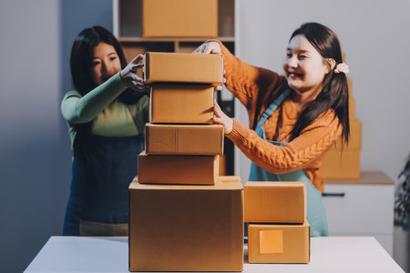 Startup SME small business entrepreneur of freelance Asian woman wearing apron using laptop and box to receive and review orders online to prepare to pack sell to customers, online sme business ideas.の写真素材