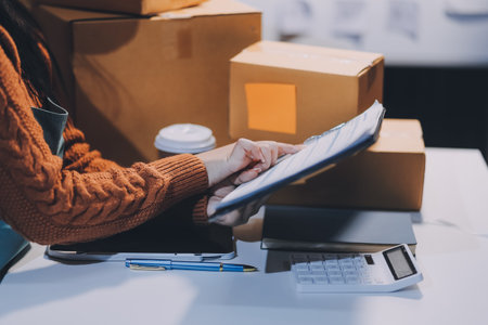 Startup SME small business entrepreneur of freelance Asian woman wearing apron using laptop and box to receive and review orders online to prepare to pack sell to customers, online sme business ideas.の写真素材