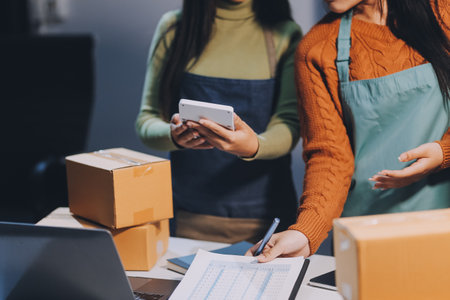 Startup SME small business entrepreneur of freelance Asian woman wearing apron using laptop and box to receive and review orders online to prepare to pack sell to customers, online sme business ideas.の写真素材