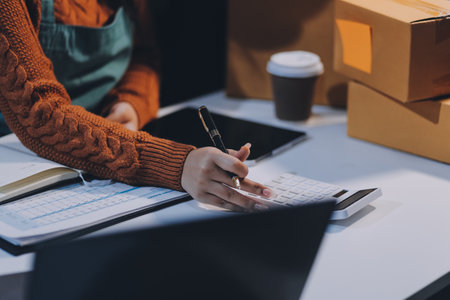 Startup SME small business entrepreneur of freelance Asian woman wearing apron using laptop and box to receive and review orders online to prepare to pack sell to customers, online sme business ideas.の写真素材
