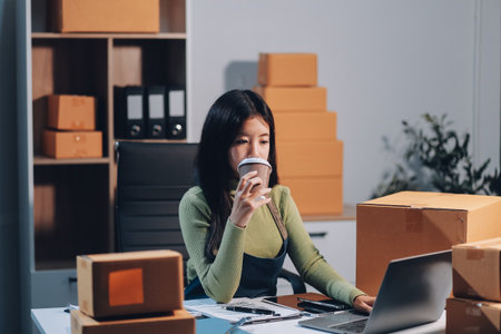 Startup SME small business entrepreneur of freelance Asian woman wearing apron using laptop and box to receive and review orders online to prepare to pack sell to customers, online sme business ideas.の写真素材