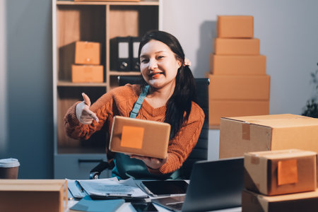Startup SME small business entrepreneur of freelance Asian woman wearing apron using laptop and box to receive and review orders online to prepare to pack sell to customers, online sme business ideas.の写真素材