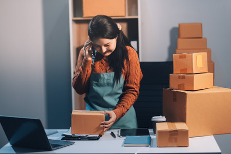 Startup SME small business entrepreneur of freelance Asian woman wearing apron using laptop and box to receive and review orders online to prepare to pack sell to customers, online sme business ideas.の写真素材