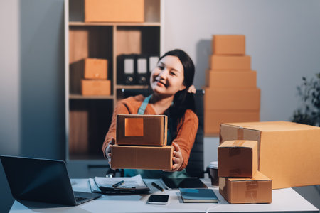 Startup SME small business entrepreneur of freelance Asian woman wearing apron using laptop and box to receive and review orders online to prepare to pack sell to customers, online sme business ideas.の写真素材