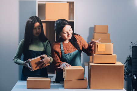 Startup SME small business entrepreneur of freelance Asian woman wearing apron using laptop and box to receive and review orders online to prepare to pack sell to customers, online sme business ideas.の写真素材