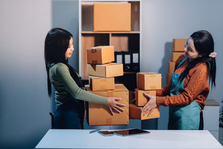 Startup SME small business entrepreneur of freelance Asian woman wearing apron using laptop and box to receive and review orders online to prepare to pack sell to customers, online sme business ideas.の写真素材